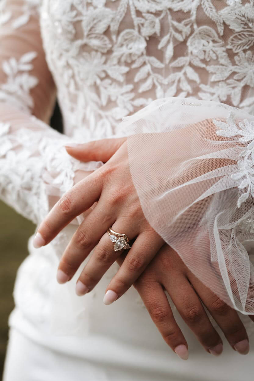 Bride’s hands in lace gown showcasing diamond engagement and wedding rings at Ideal Jewelers Frederick MD