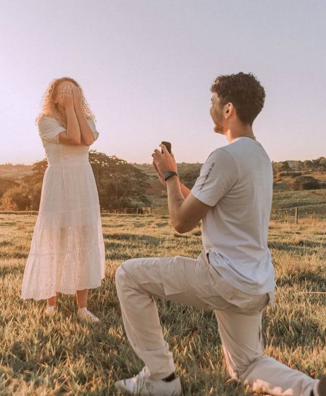 Man proposing with engagement ring at sunset in a scenic field