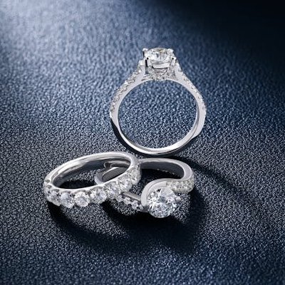 Trio of diamond engagement and wedding rings on textured navy background Ideal Jewelers home page category header